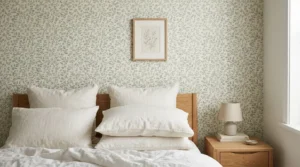 Bedroom bed wall in small sage botanical wallpaper, centred above white linen pillows, oak bedside table, soft daylight, no people