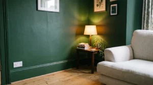 Deep green painted wall with warm lamp light and pale sofa in a living room.